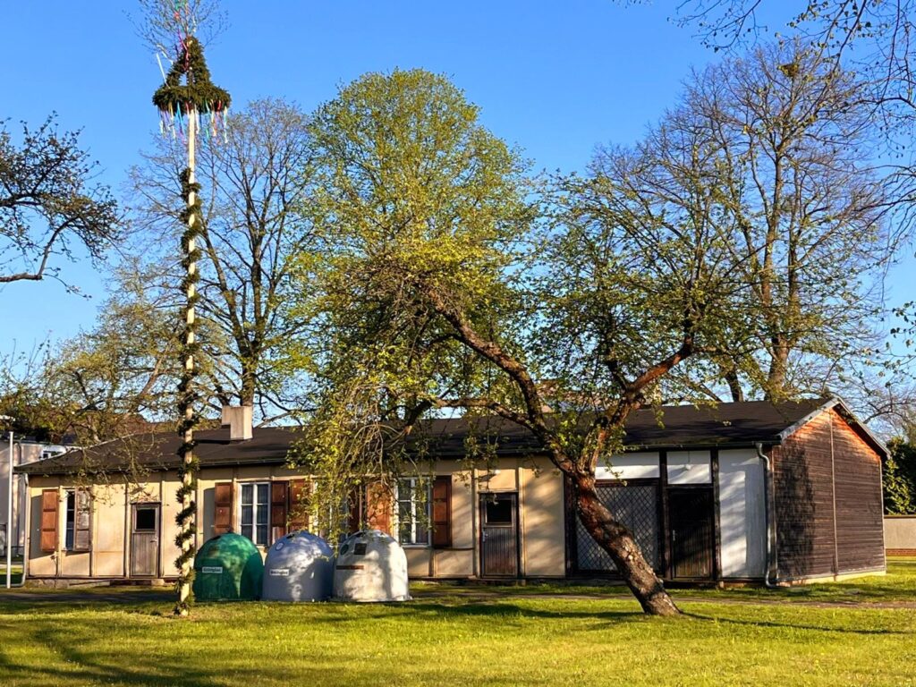 Ein deutscher Maibaum vor einem einstöckigen Gebäude.